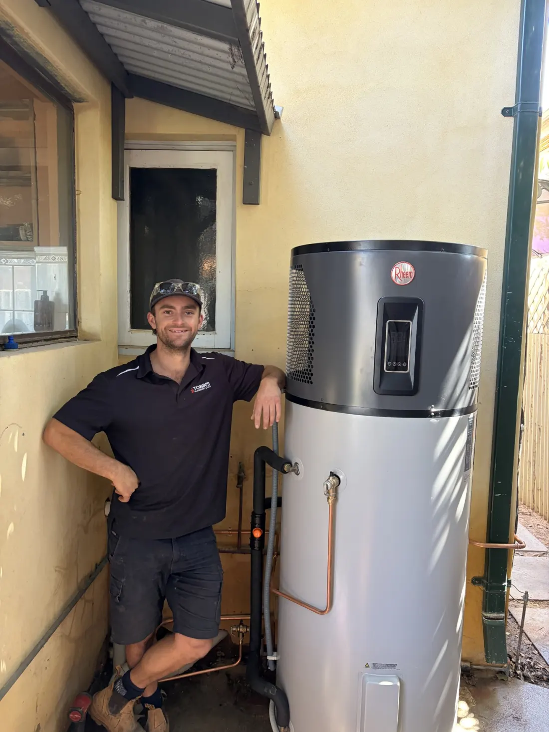 Remy Tobin standing beside a Rheem heat pump hot water system